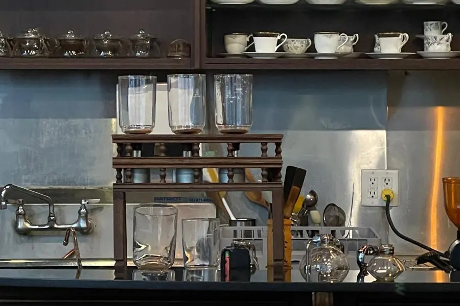 Classic wooden shelves displaying vintage coffee cups and siphon coffee equipment inside La Cuisson Café in Vancouver.