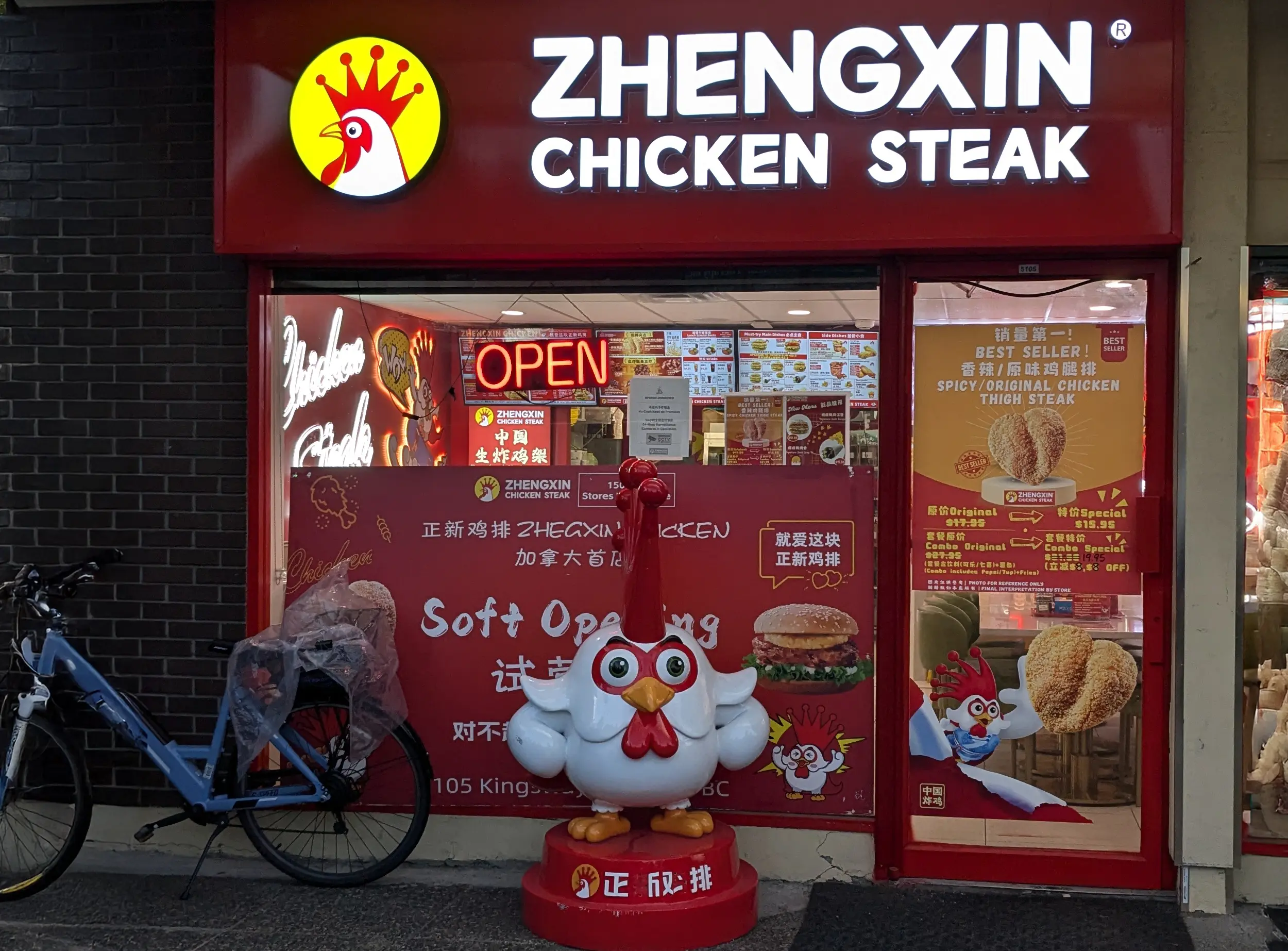 Bright red storefront of Zhengxin Chicken Steak featuring a large chicken statue outside, promotional posters on the windows, and an illuminated ‘OPEN’ sign.