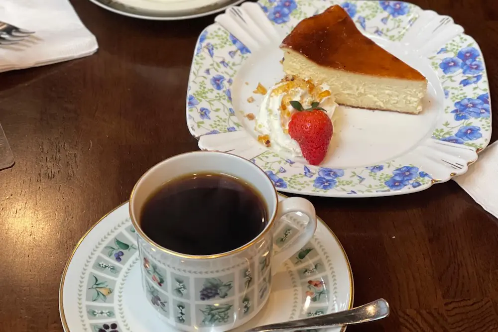 Siphon coffee served in an elegant vintage cup with a slice of cheesecake at La Cuisson Café in Vancouver.