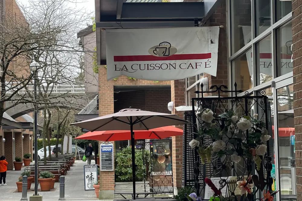 Exterior of La Cuisson Café in Kerrisdale, Vancouver, featuring a hanging café sign and outdoor umbrellas.